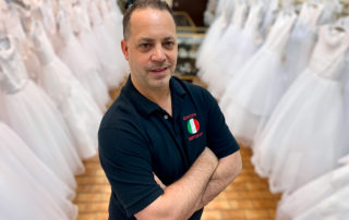 Paul Governali stands arms crossed amidst aisles of communion dresses