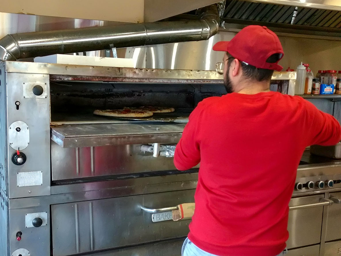 Man putting pizza into oven